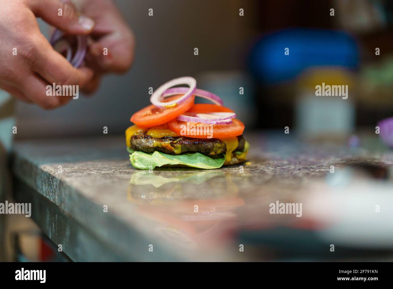 Close up on hands of unknown caucasian man chef making burger on the counter-top in the kitchen at restaurant or at home Stock Photo