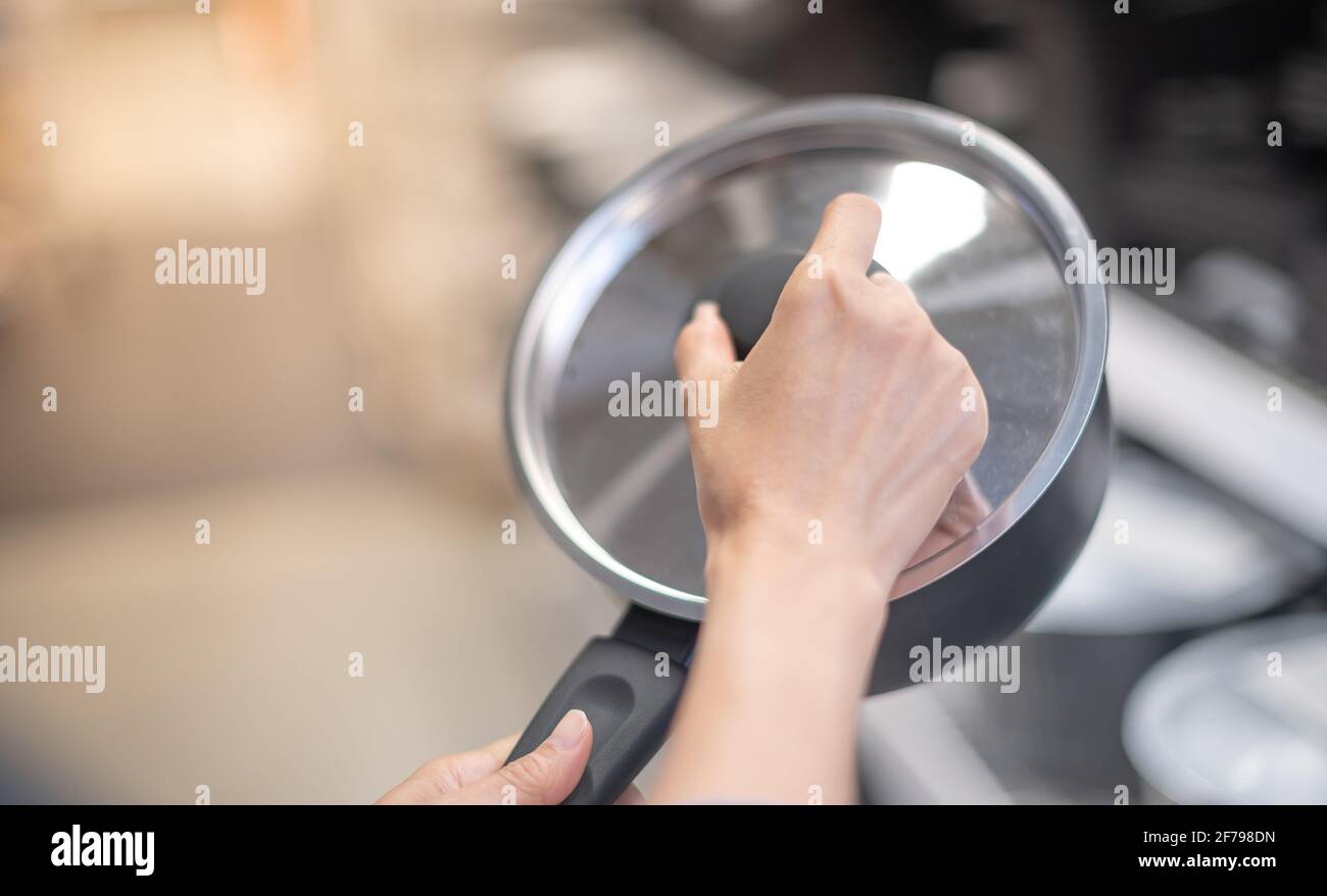 Female hand holding new empty small kitchen saucepan covered with transparent glass lid. Stock Photo