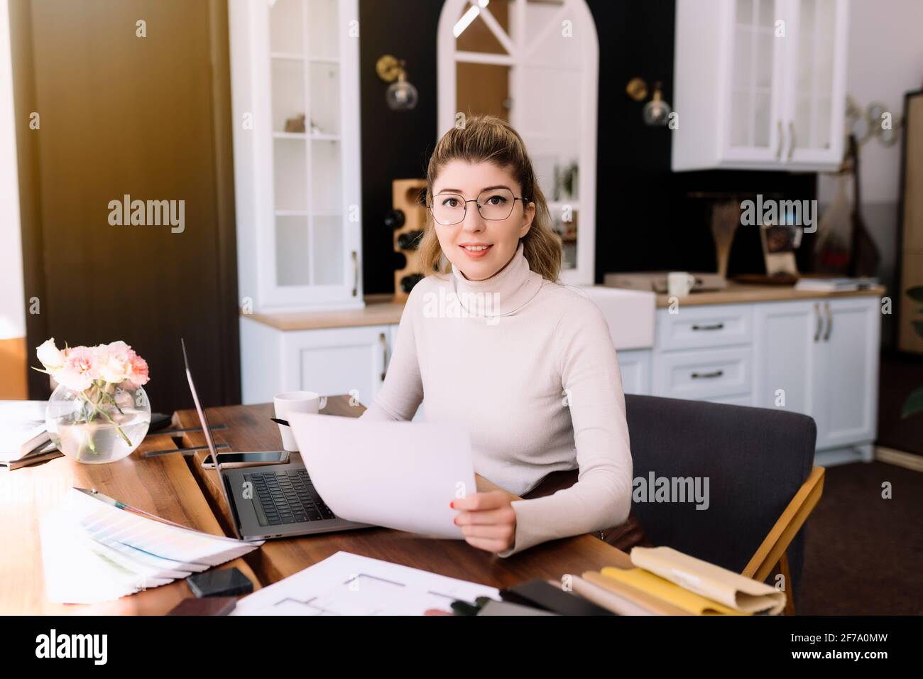 An interior designer is working on a new project, woman holding paper plan with pen. Considering the decision. Thinking about new design. Laptop on th Stock Photo