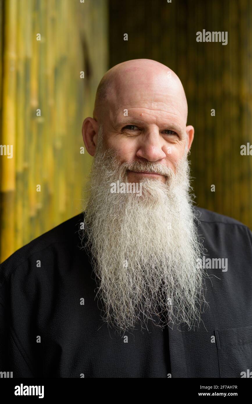 Portrait of man bald man with long gray beard outdoors against bamboo wall Stock Photo