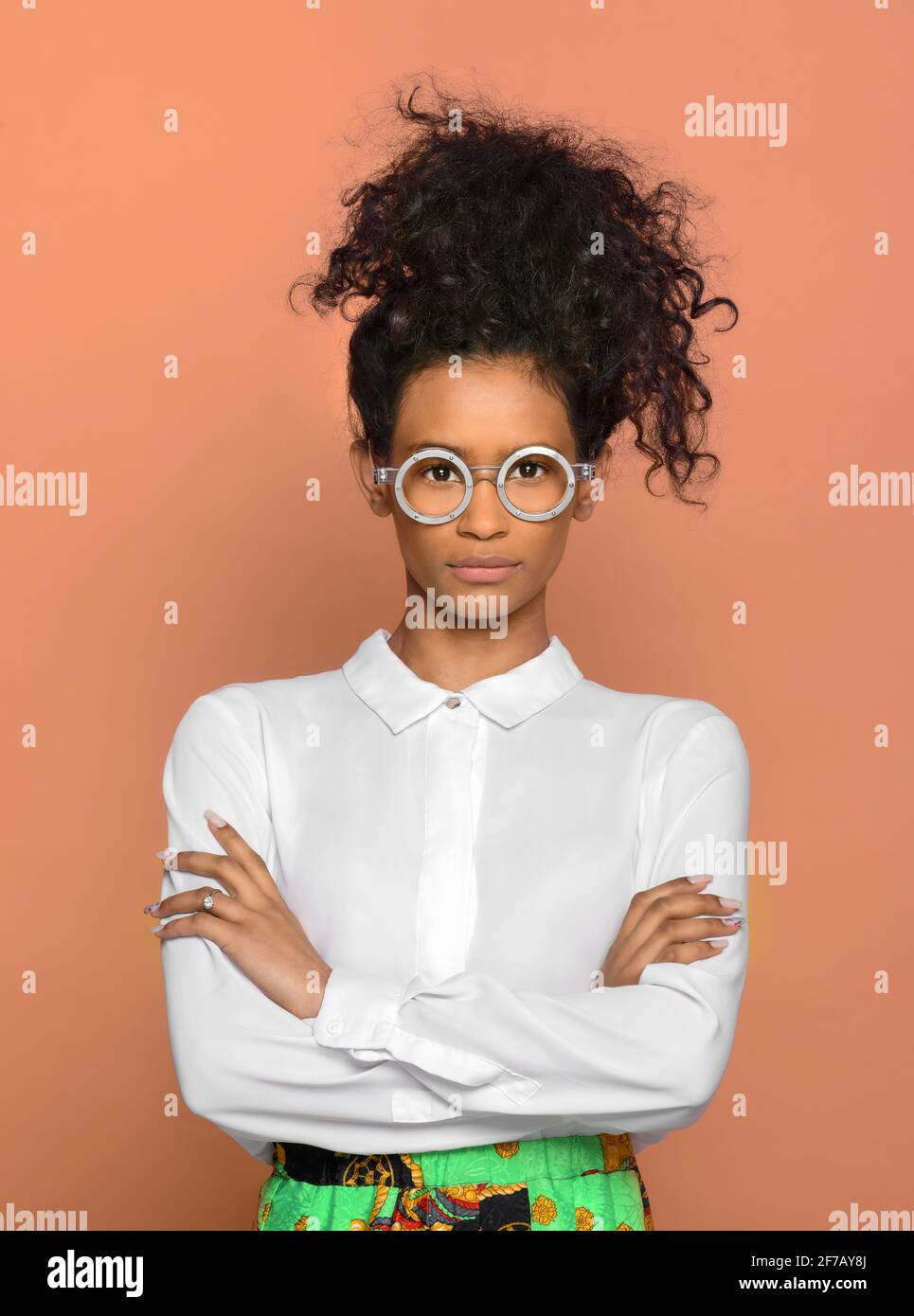 Serious confident black woman with her long curly hat tied to the top of her head standing wearing round eyeglasses staring at the camera over a studi Stock Photo