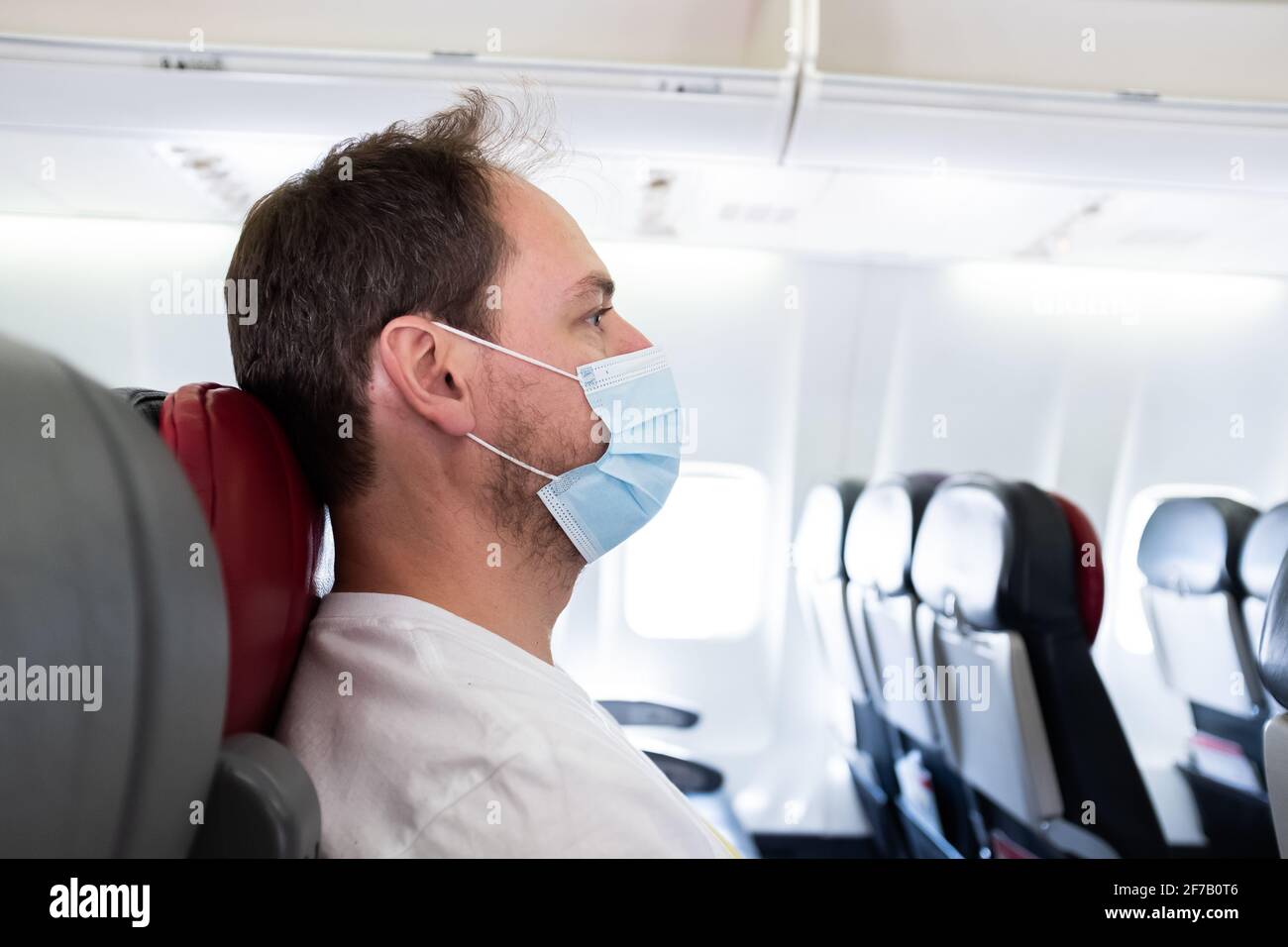Man on an airplane wearing a surgical mask traveling during the COVID-19 coronavirus pandemic Stock Photo