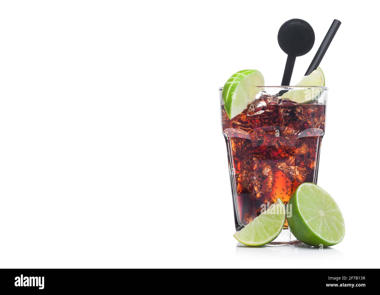 Cuba Libre Cocktail in glass with ice cubes and slices of lime with black straw and stirrer on white background with raw limes.Space for text Stock Photo