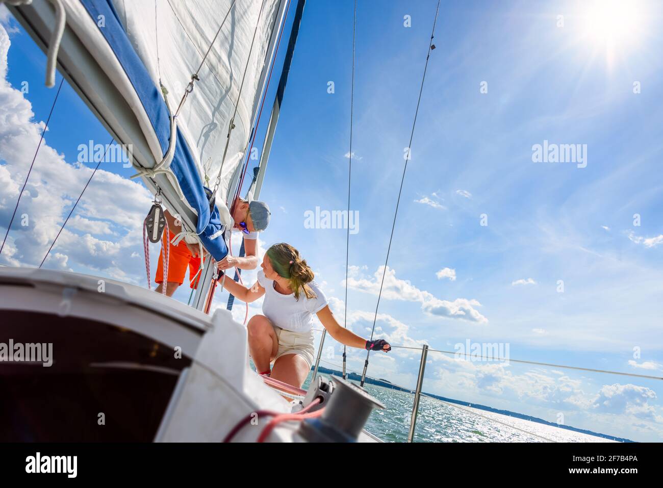 Young woman and man sailing on a yacht. Sailboat crewmember trimming main sail during sail on vacation in summer season Stock Photo