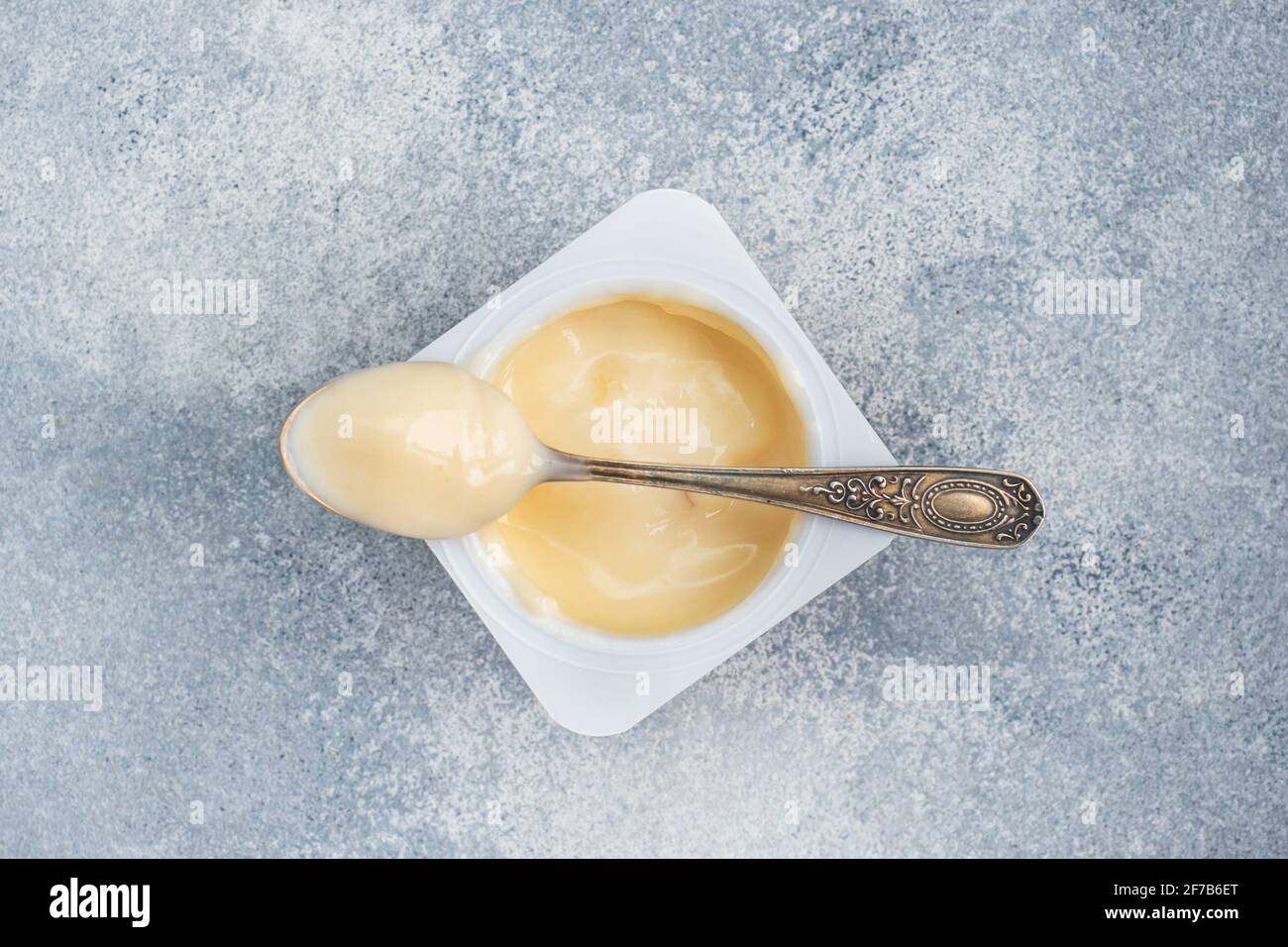 Milk fruit yogurt in an open package and a teaspoon. Gray concrete background, copy space Stock Photo