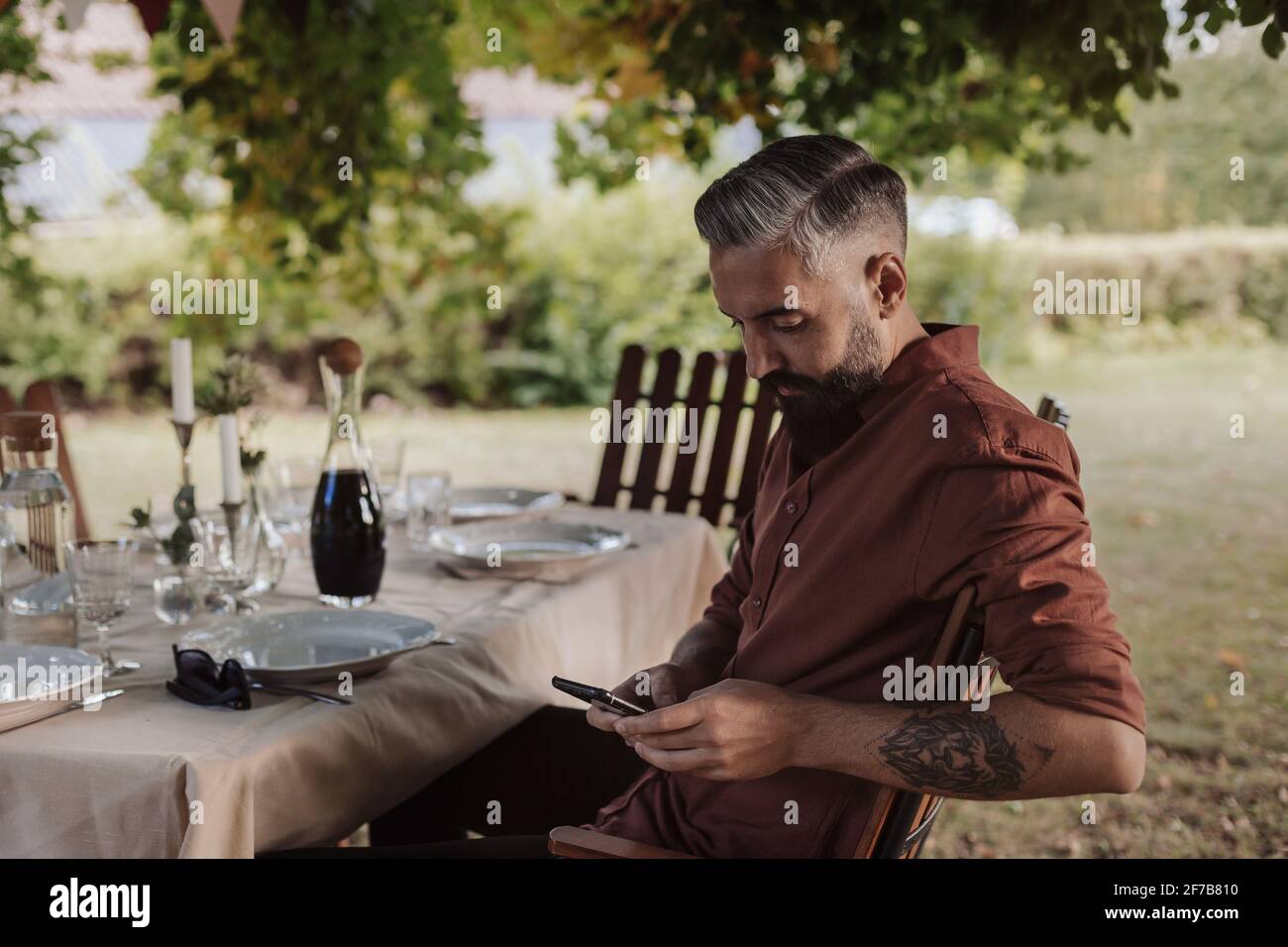 Man sitting at table in garden and using cell phone Stock Photo