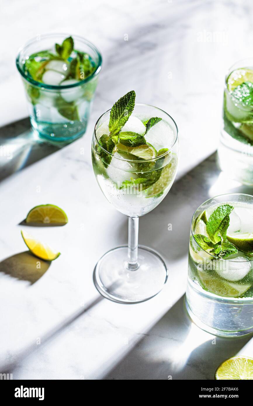 Mojito cocktail with mint and lime in different glasses, white marble background. Refreshing drink with lime and mint in glasses. Stock Photo