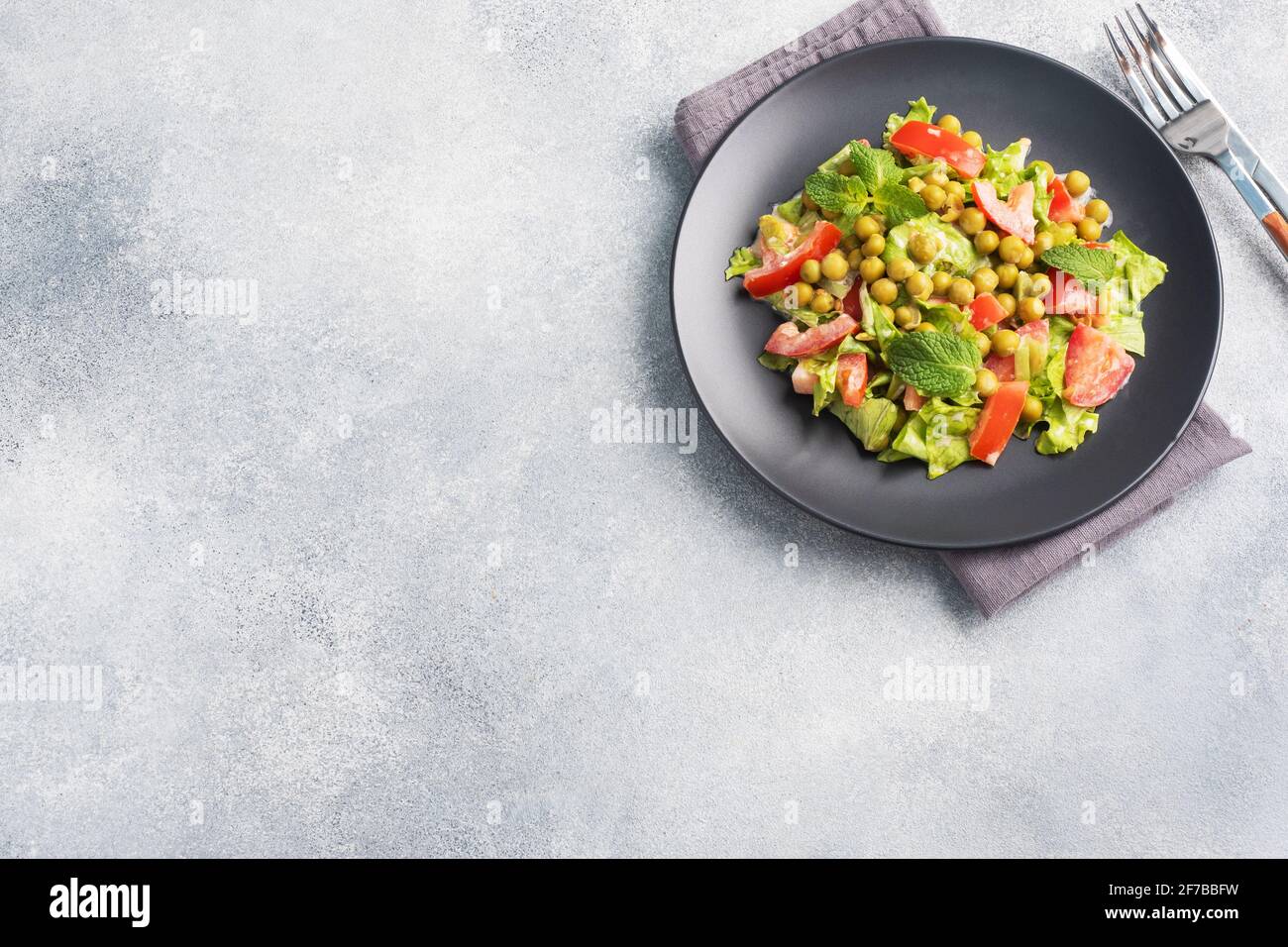Salad of green tomato leaves and canned peas seasoned with sauce on a black plate. Spring fresh diet salad top view copy space. Stock Photo