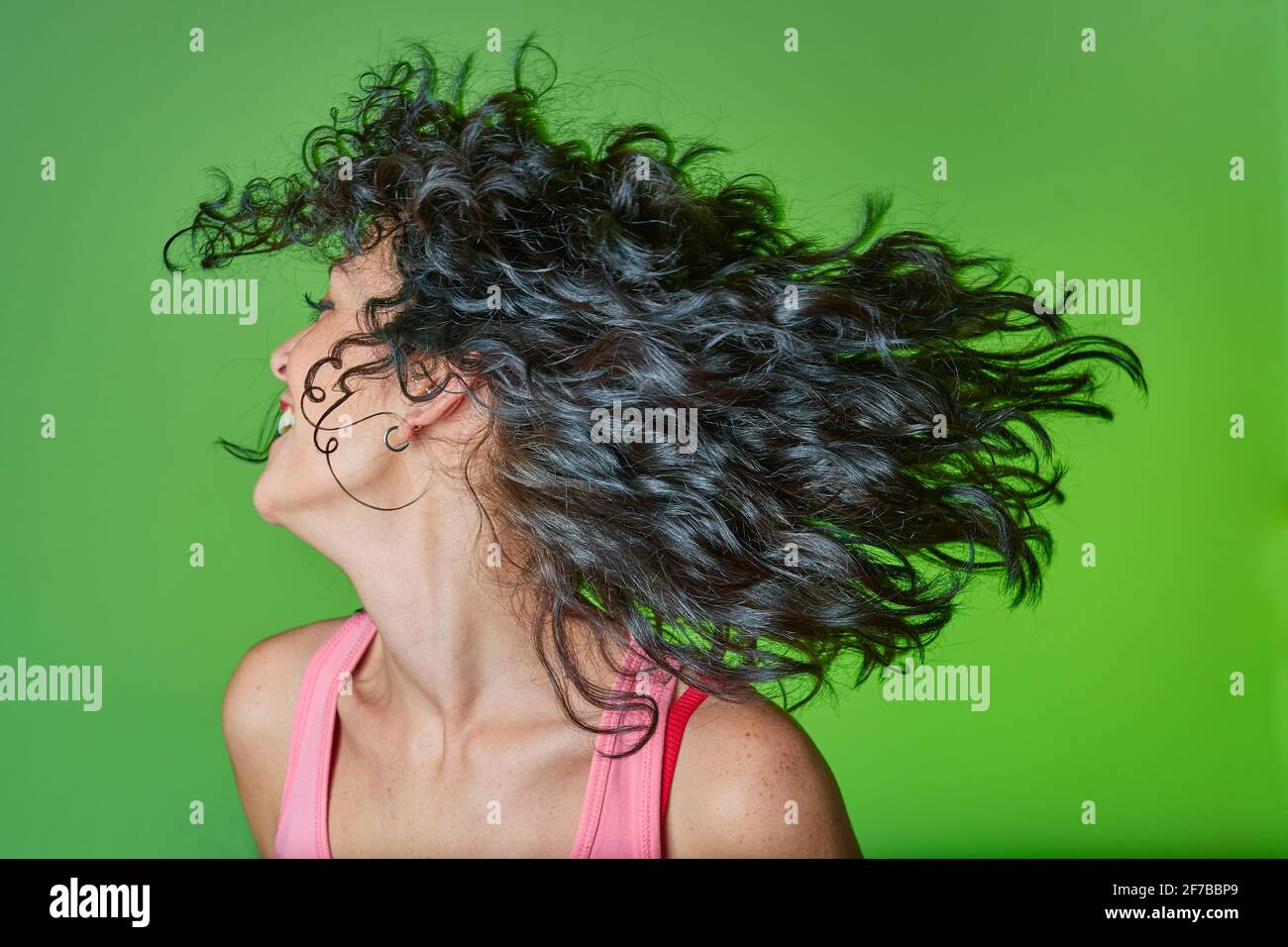 smiling young woman with curly black hair following curly girl method for caring for her curls and hair. hair care concept. green background. Stock Photo