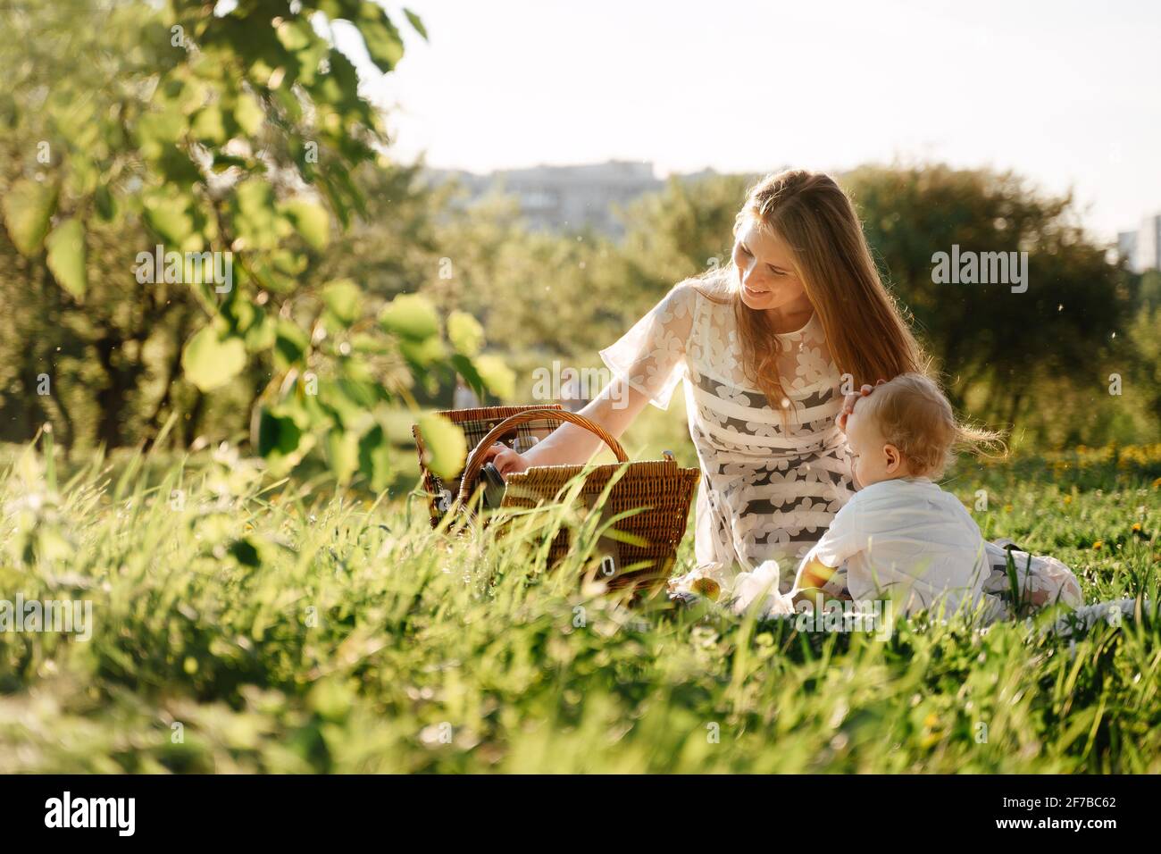 Parents mom and daughter at a picnic sit on green grass in the field. Stock Photo