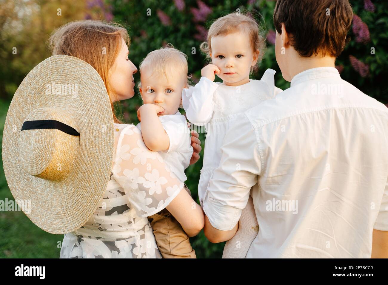 Young happy parents hold little children brother and sister in the park, children look at the camera. Stock Photo