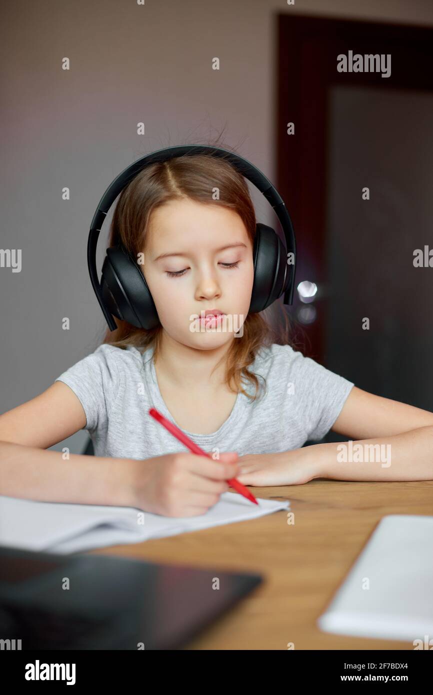 Cute little girl with headphones using laptop to study at home