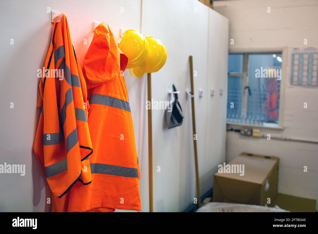 High visibility protective clothing and hard hats hanging up in a warehouse for easy access for the workers. Warehouse, stores, safety gear concept Stock Photo