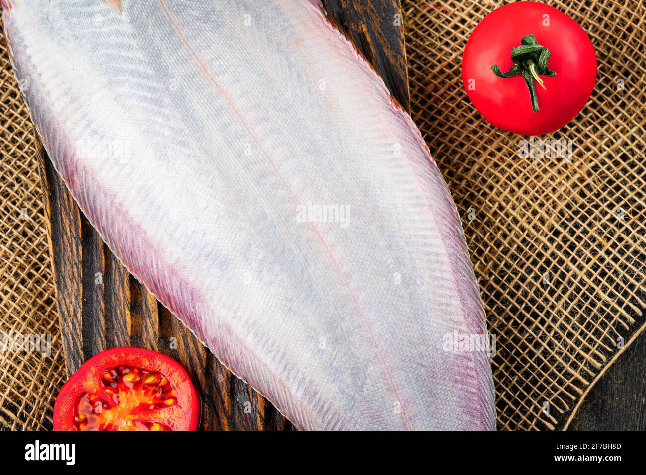 Raw fresh sole fish with tomatoes on a wooden cutting board. White belly of a fish Stock Photo
