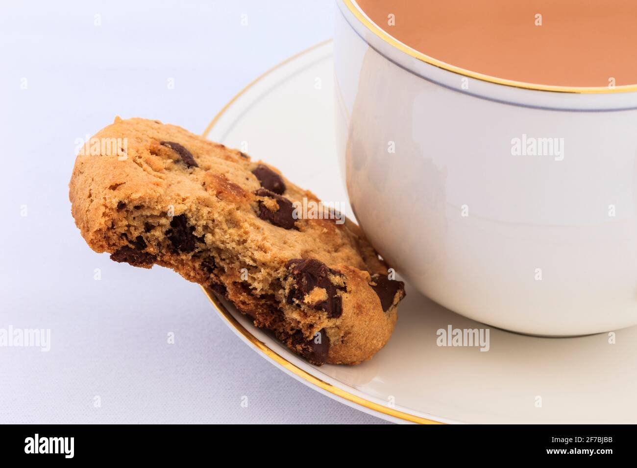 Cup of English tea and a chocolate chip biscuit with a bite taken out on the saucer. Stock Photo