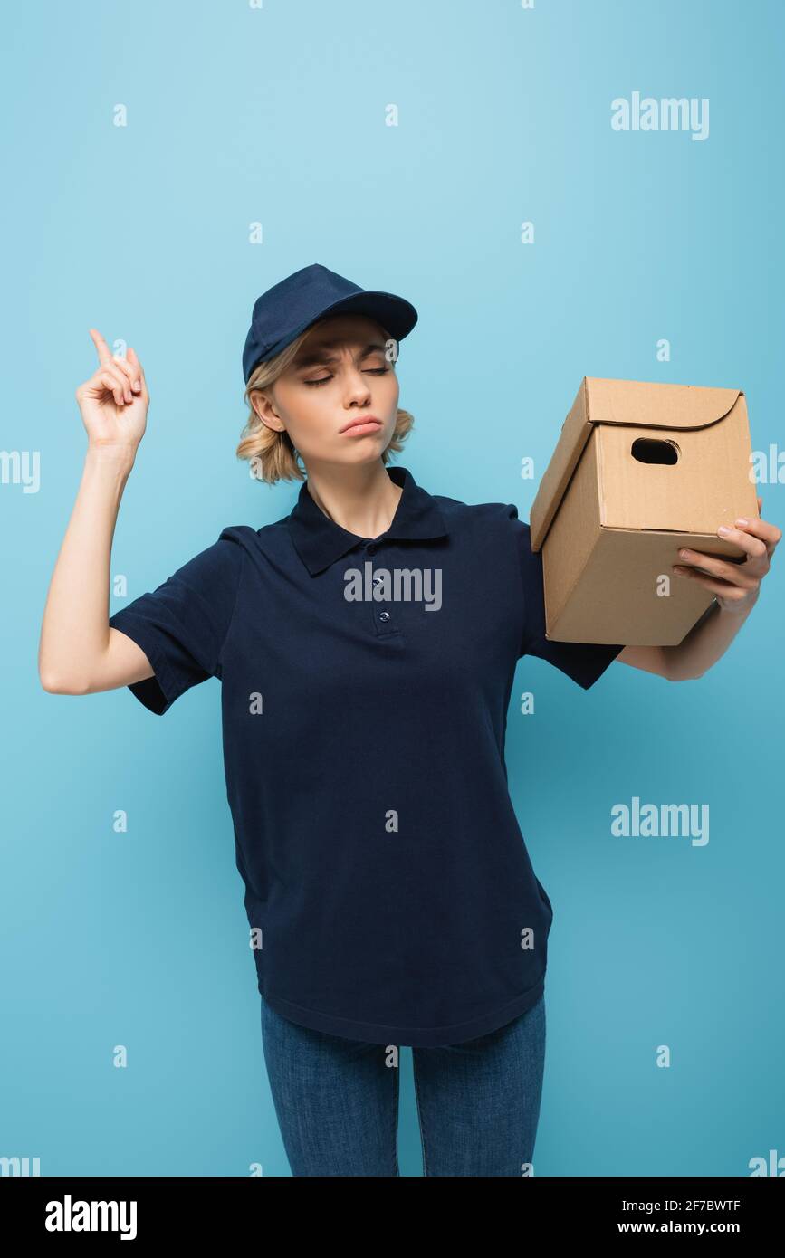 serious courier holding parcel and pointing up with finger on blue ...