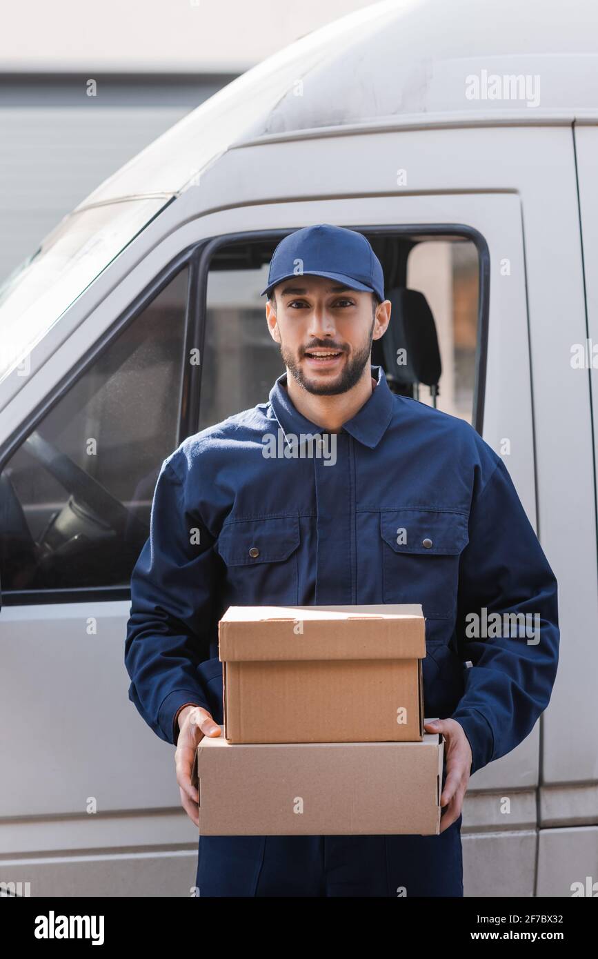 cheerful muslim postman holding parcels while standing near car outdoors Stock Photo