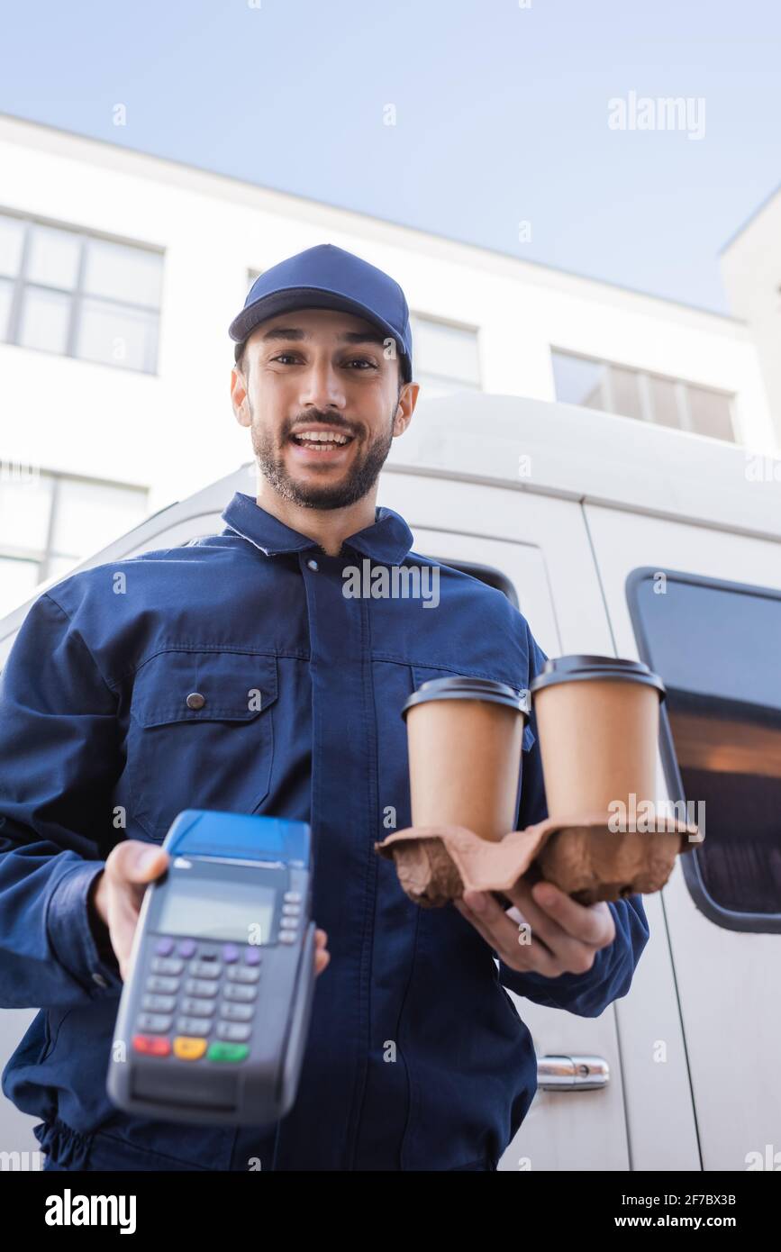 happy muslim delivery man holding paper cups and payment terminal on