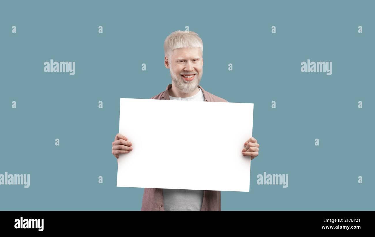 Look here. Excited albino man holding blank poster with copy space on studio background, panorama, free space Stock Photo