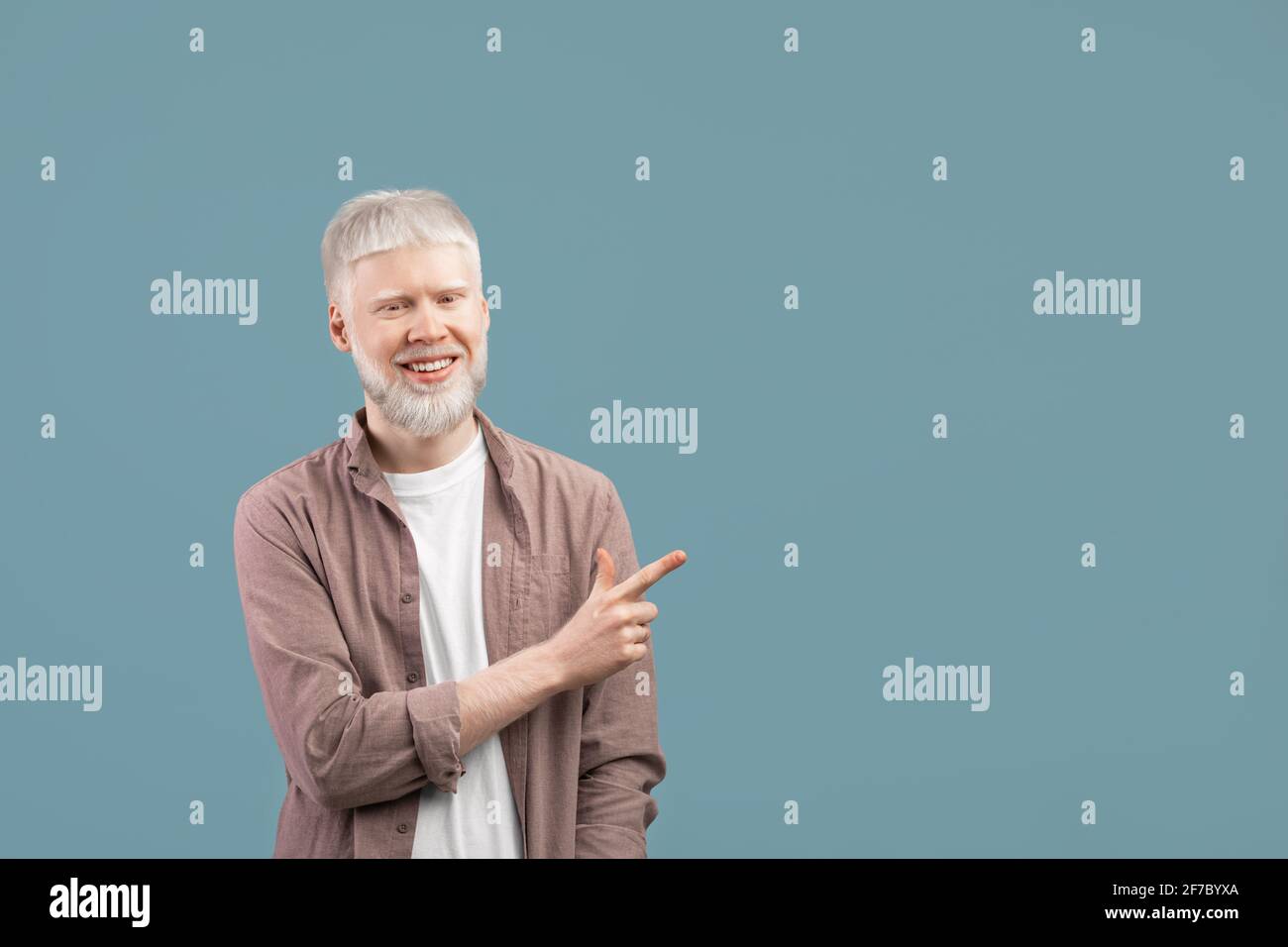 Cool offer. Confident albino man pointing at free space on turquoise studio background and smiling to camera Stock Photo