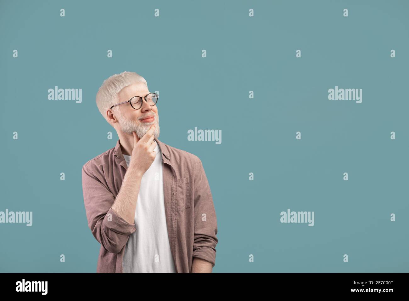 Pensive albino guy thinking over decision, looking at empty space over turquoise studio background Stock Photo