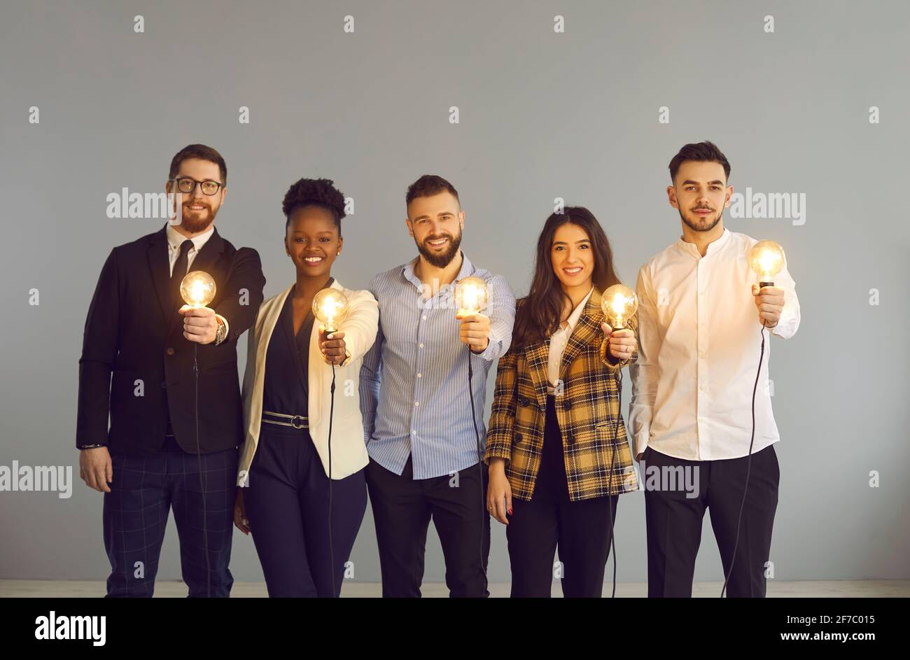 Diverse business team holding light idea bulb stand over grey studio background Stock Photo