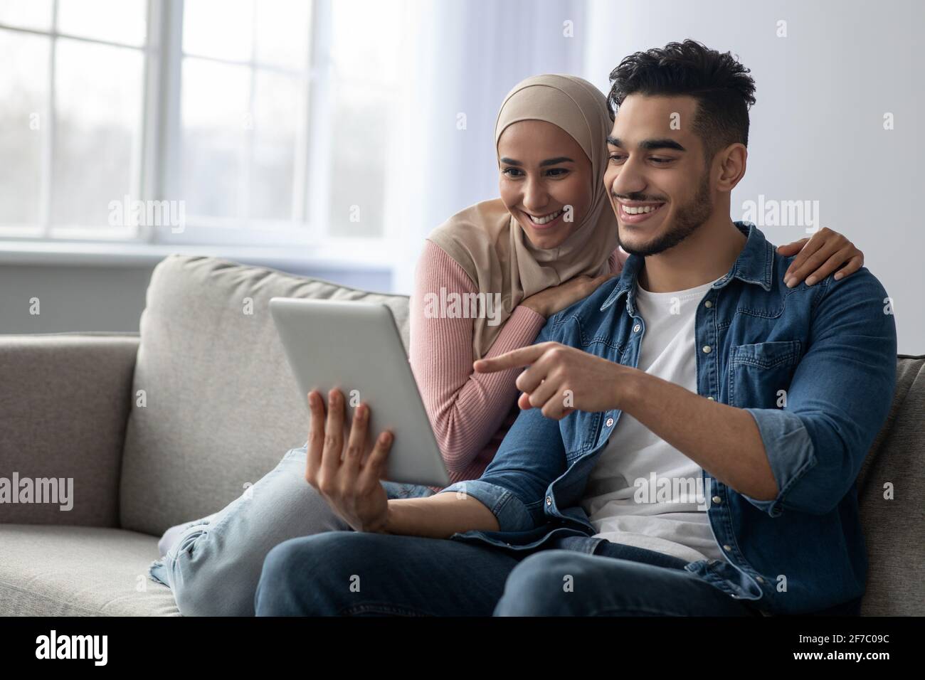 Cheerful arab guy showing something girlfriend on Internet, using pad Stock Photo