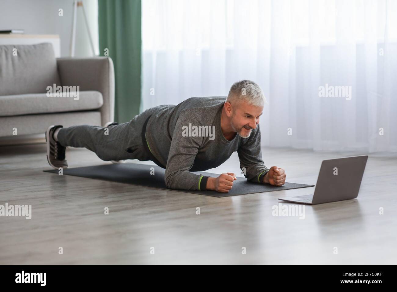 Athletic mature bearded man doing exercises at home, using laptop Stock Photo