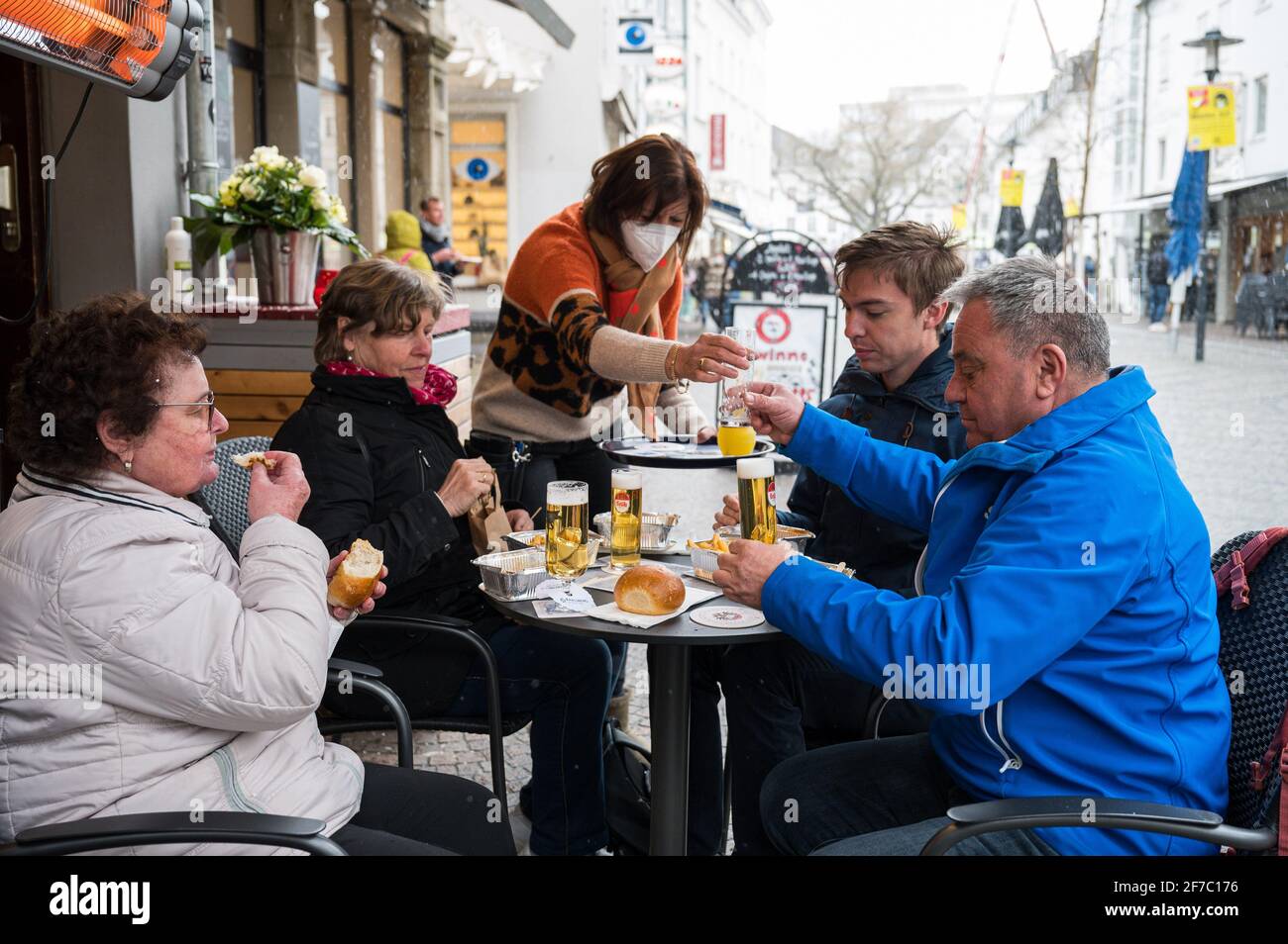 06 April 2021, Saarland, Saarbrücken: Landlady Monika Müller (m) brings drinks to her guests sitting in front of her pub 'Glühwürmchen' in the city centre. Since 06.04.2021, restaurateurs have been allowed to reopen their outdoor restaurants under certain conditions as part of the Saarland Model. Photo: Oliver Dietze/dpa Stock Photo