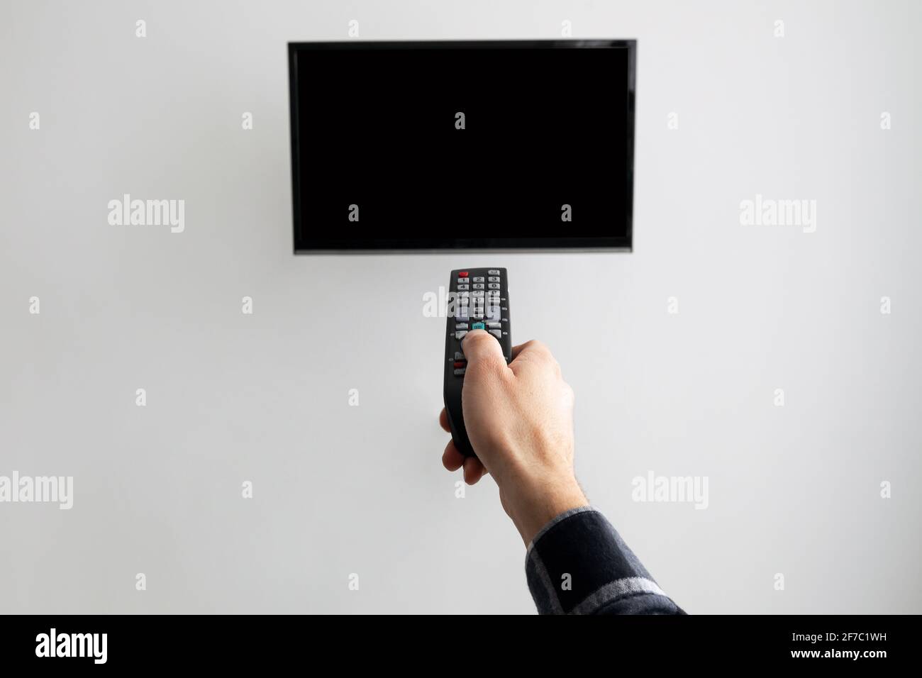 Hand Pointing Controller At Blank TV Screen On Wall Indoor Stock Photo