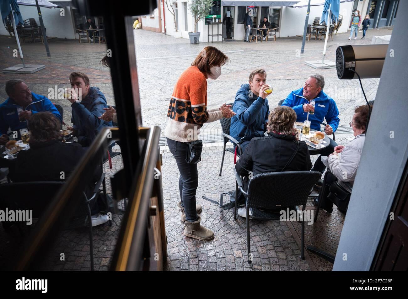 06 April 2021, Saarland, Saarbrücken: Landlady Monika Müller (M) brings drinks to her guests sitting in front of her pub 'Glühwürmchen' in the city centre. Since 06.04.2021, restaurateurs have been allowed to reopen their outdoor restaurants under certain conditions within the framework of the Saarland Model. Photo: Oliver Dietze/dpa Stock Photo