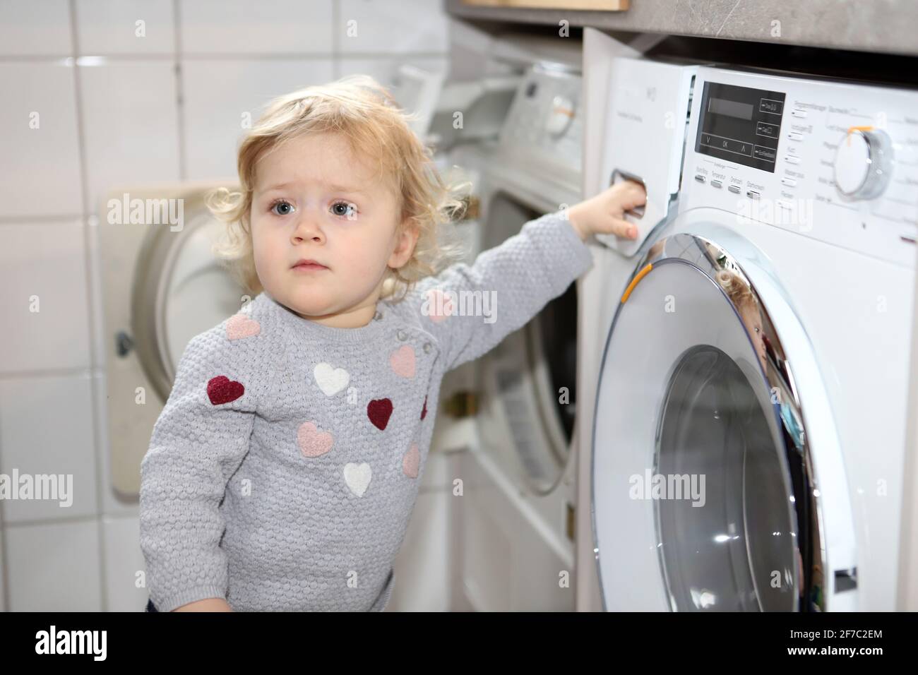 kleines Mädchen hält sich mit einer Hand an einer Waschmaschine fest - little girl holding on to washing machine with one hand Stock Photo