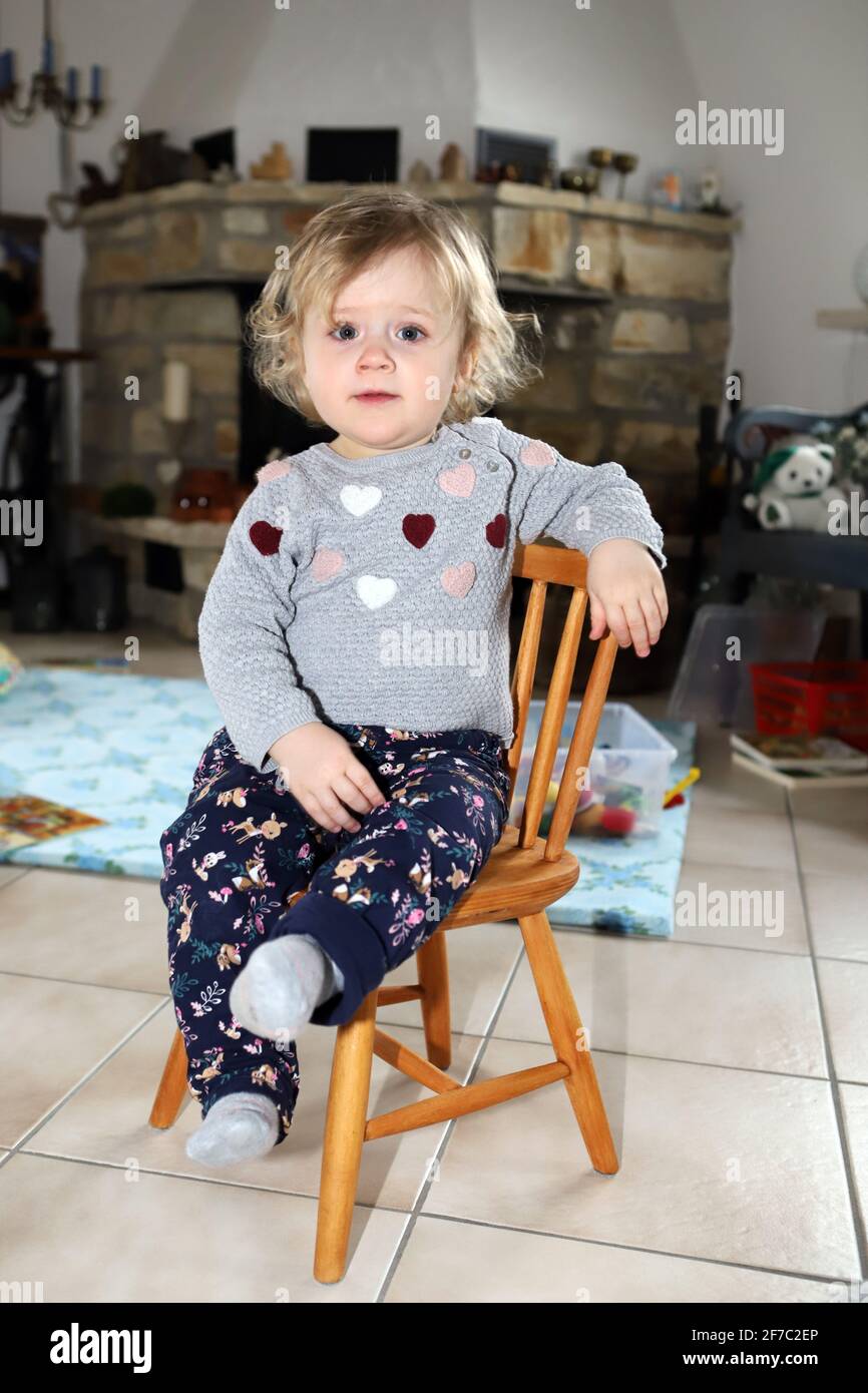kleines Mädchen sitzt im Wohnzimmer auf einem Kinderstuhl aus Holz - little girl sitting on a wooden child chair in living room Stock Photo