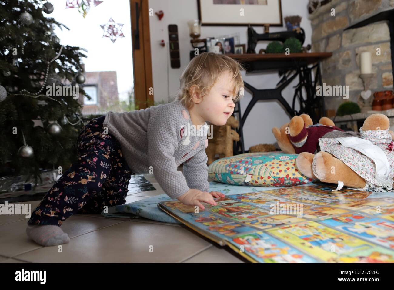 kleines Mädchen betrachtet auf dem Boden des Wohnzimmers ein großes Bilderbuch - little girl looking at big picture book on the floor of living room Stock Photo