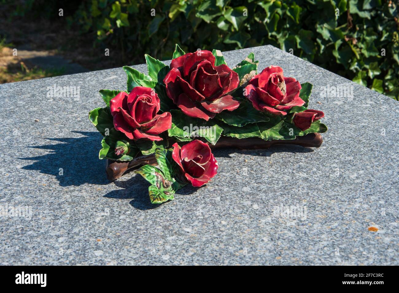 Red ceramic rose flowers on tomb in cemetery. France. Traditional