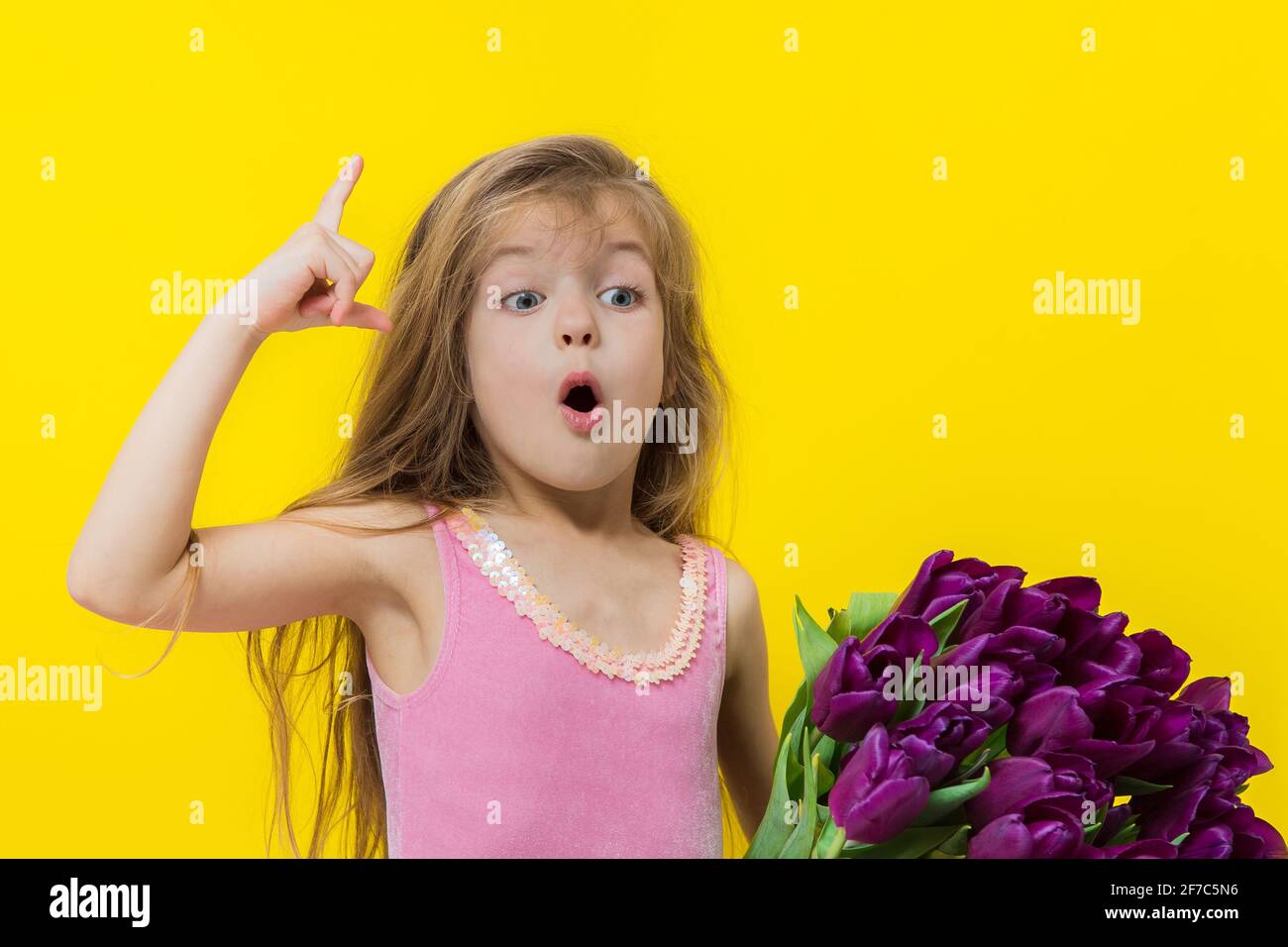Cute little girl holding bunch of flowers on the yellow background in the studio. Stock Photo