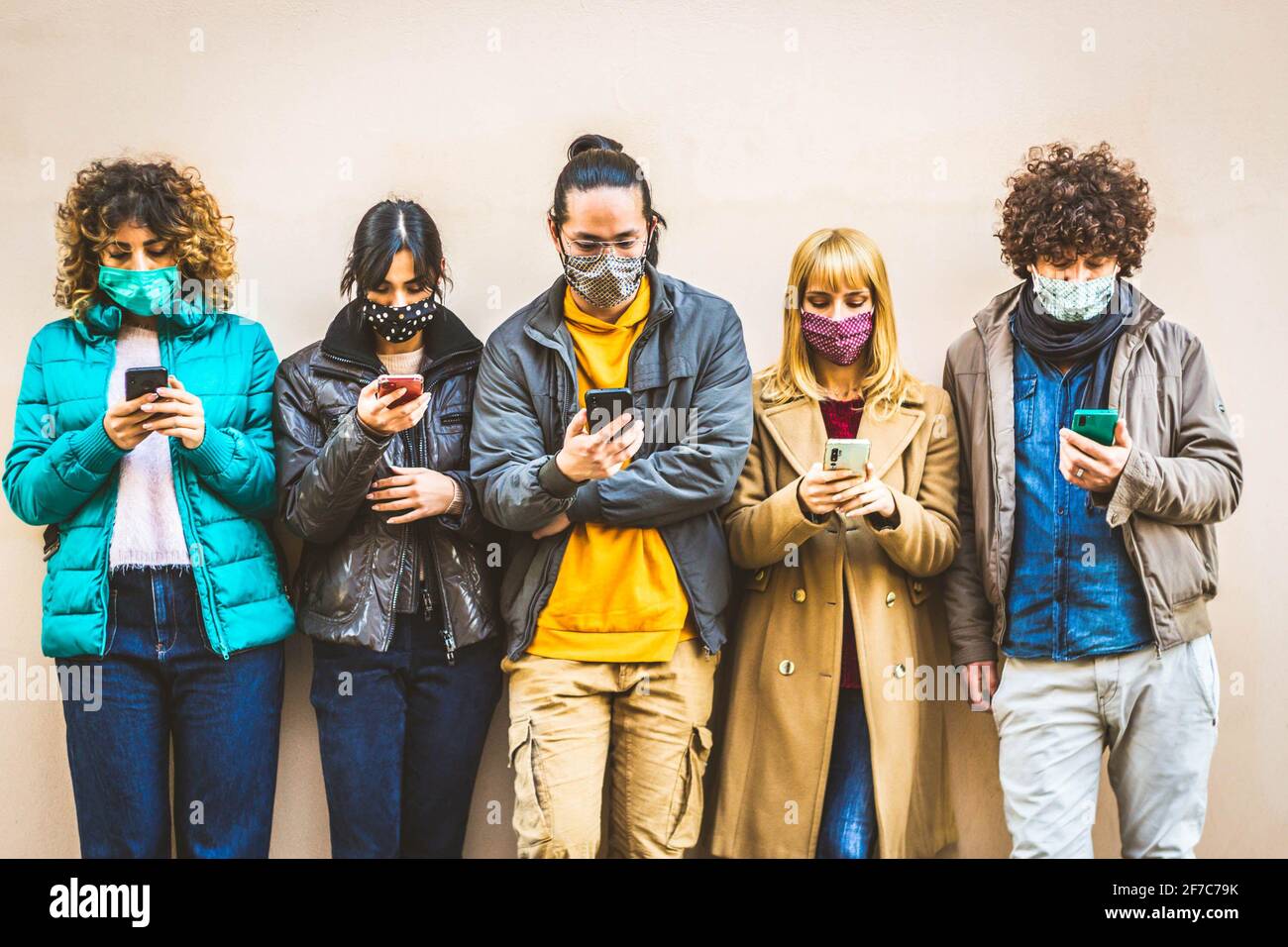 Group of young people covered by face masks using smartphone mobile device - New normal concept with friends on social media - People and technology c Stock Photo