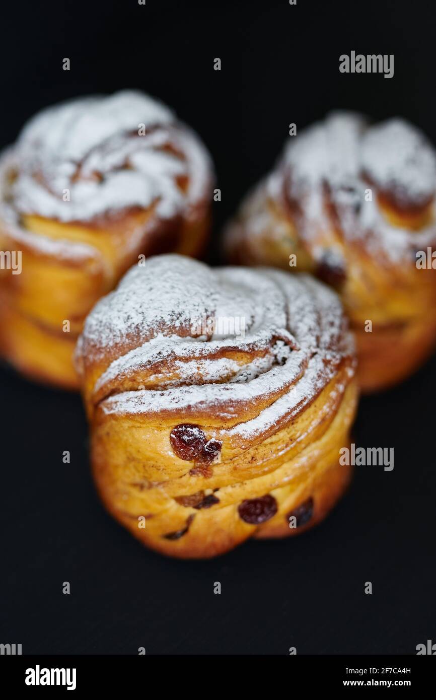 Fresh Easter pie or bakery concept. Cute cruffins with raisins and white sugar powder on it on black background. Vertical image. High quality photo Stock Photo
