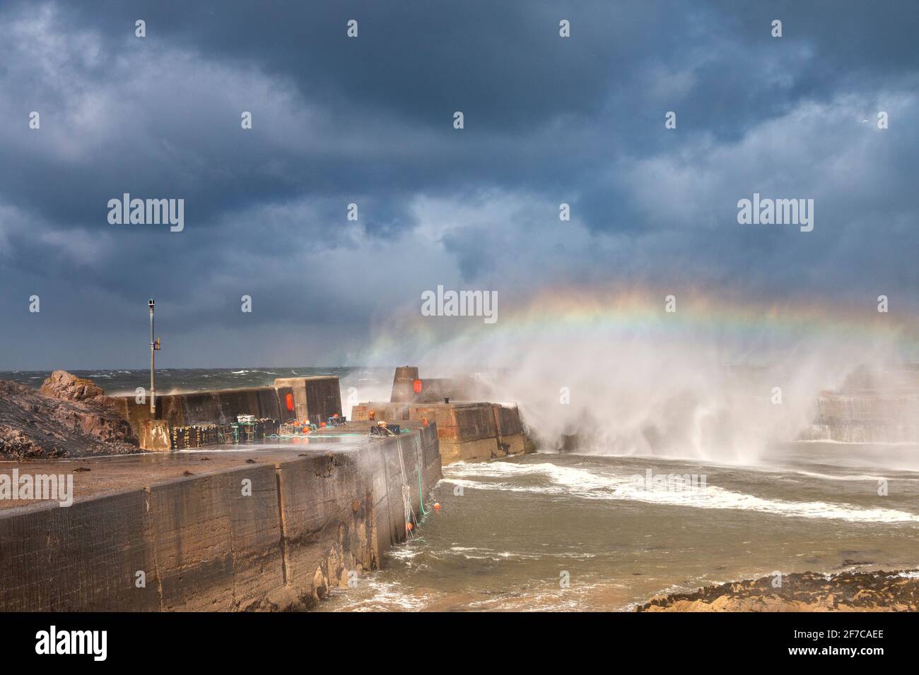 PORTKNOCKIE MORAY COAST SCOTLAND SEVERE STORM AND TURBULENT WINDS AND  WAVES BREAKING OVER HARBOUR WALL WITH A RAINBOW IN THE SPRAY Stock Photo