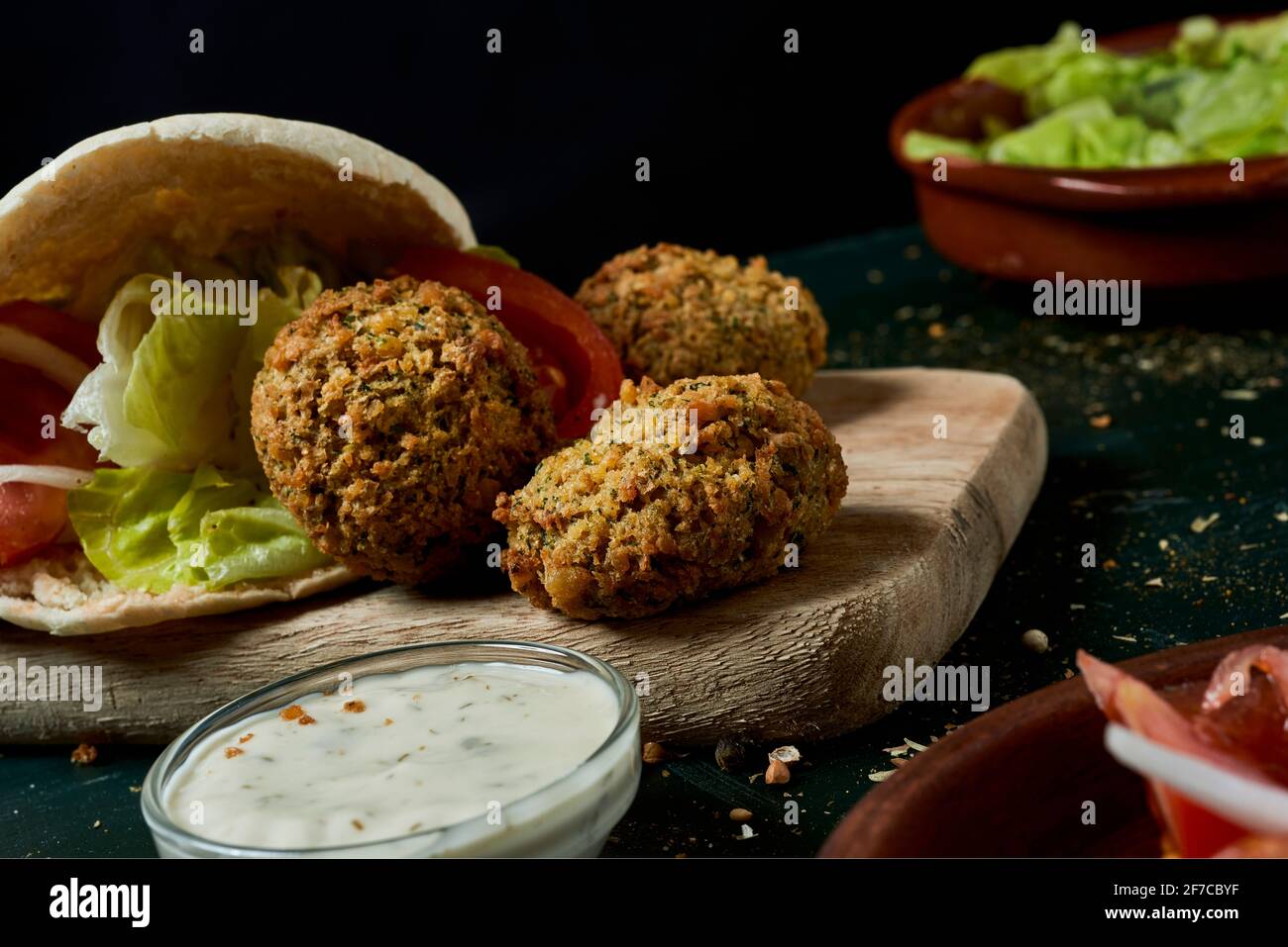 closeup of some falafel out from a pita bread, filled with some chopped lettuce, onion and tomato, on a rustic green wooden table Stock Photo
