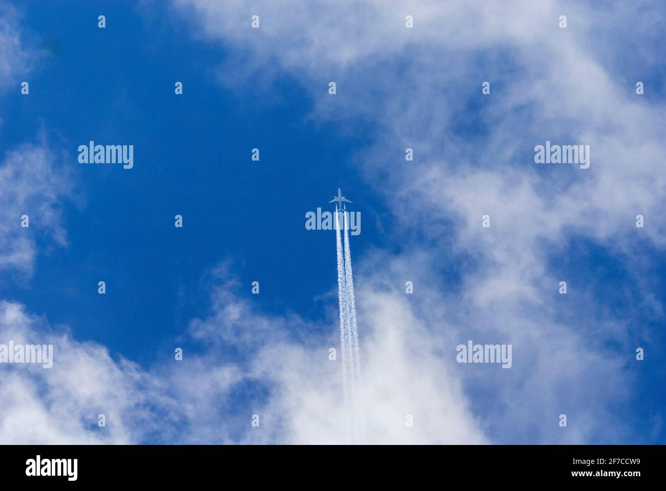 Twin engined jet aeroplane leaves contrails across deep blue sky with white clouds. Stock Photo