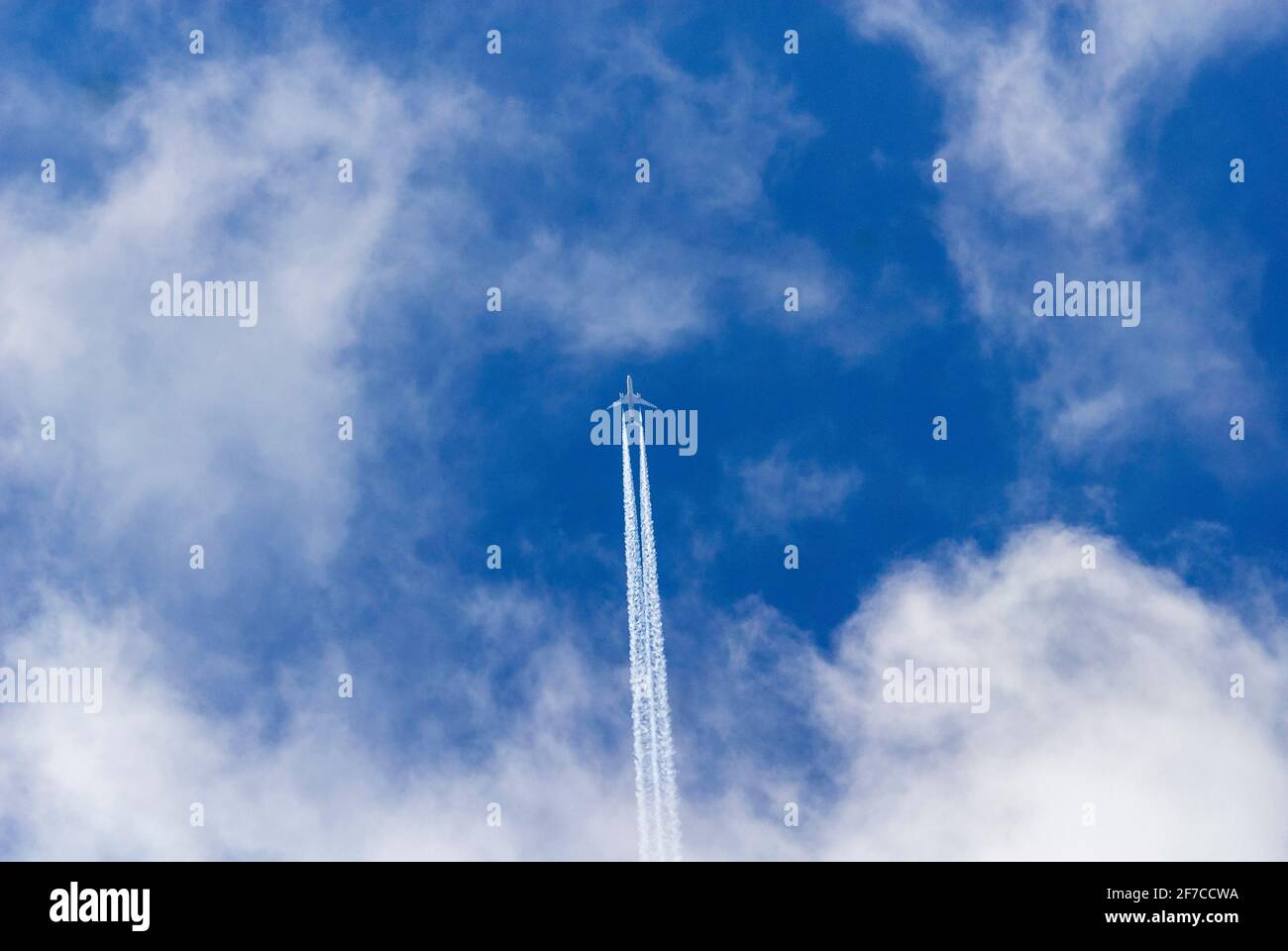 Twin engined jet aeroplane leaves contrails across deep blue sky with white clouds. Stock Photo