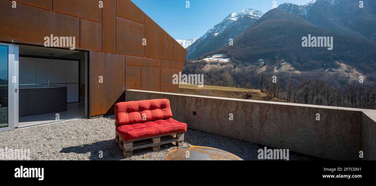 Modern house exteriors with veranda. Red sofa overlooking the mountains of Switzerland. Concept, nobody inside Stock Photo