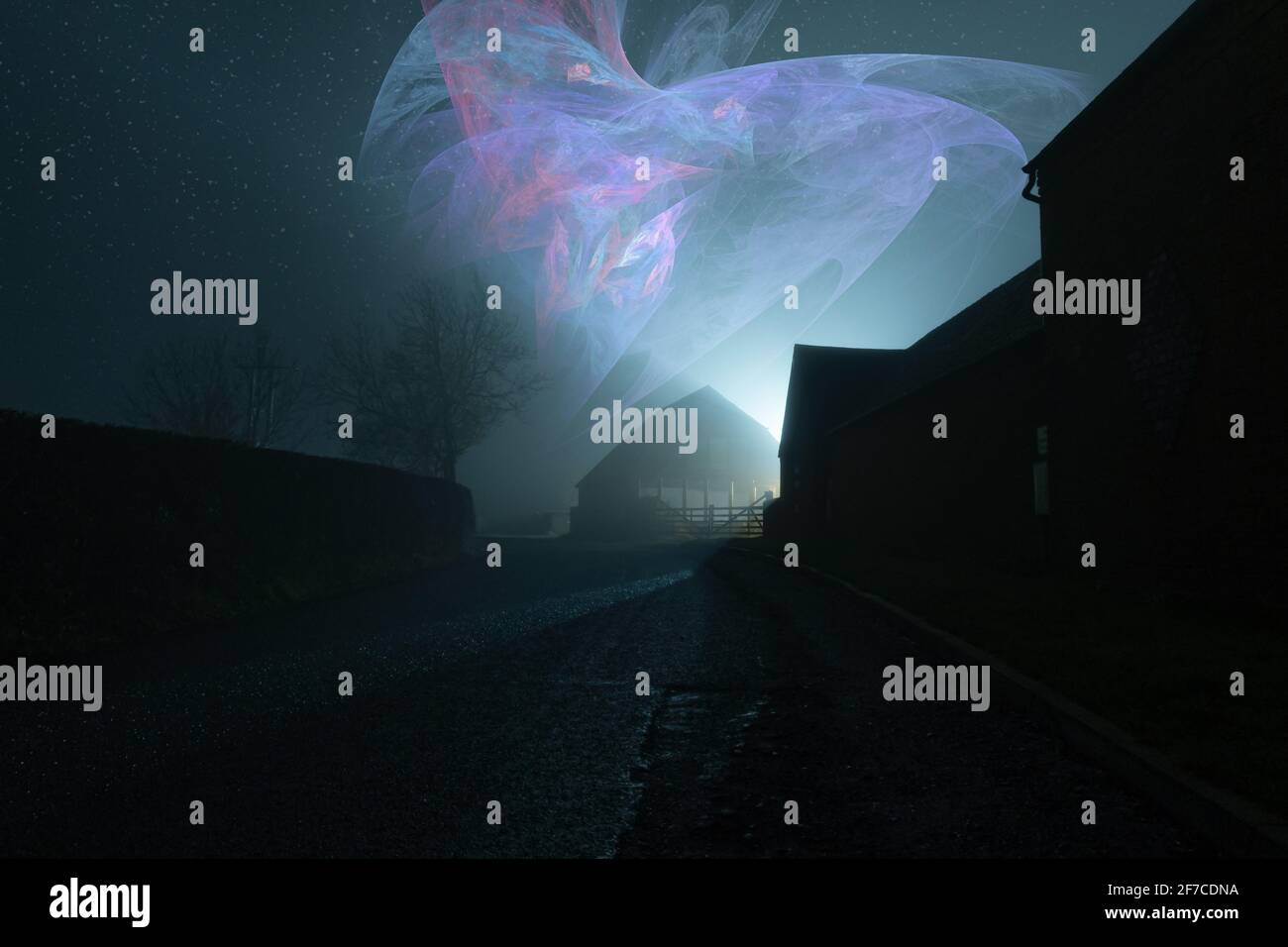A dark moody country road going into the distance, next to farm buildings with a glowing alien spaceship in the night sky Stock Photo