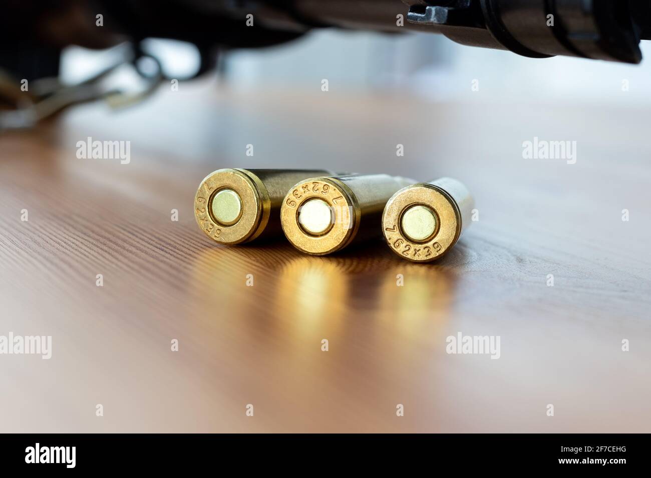 Three bullets bottom against blurred Kalashnikov assault rifle background. Cartridges 7.62 caliber for ak 47 closeup. Stock Photo