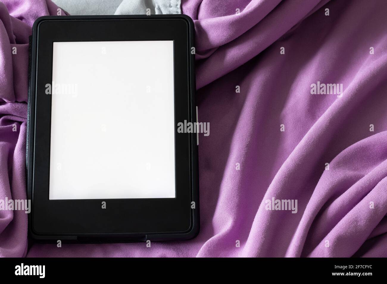 A modern black e-reader electronic book with a blank screen on a gray and purple bed. Mockup template tablet on microfiber bedding closeup Stock Photo