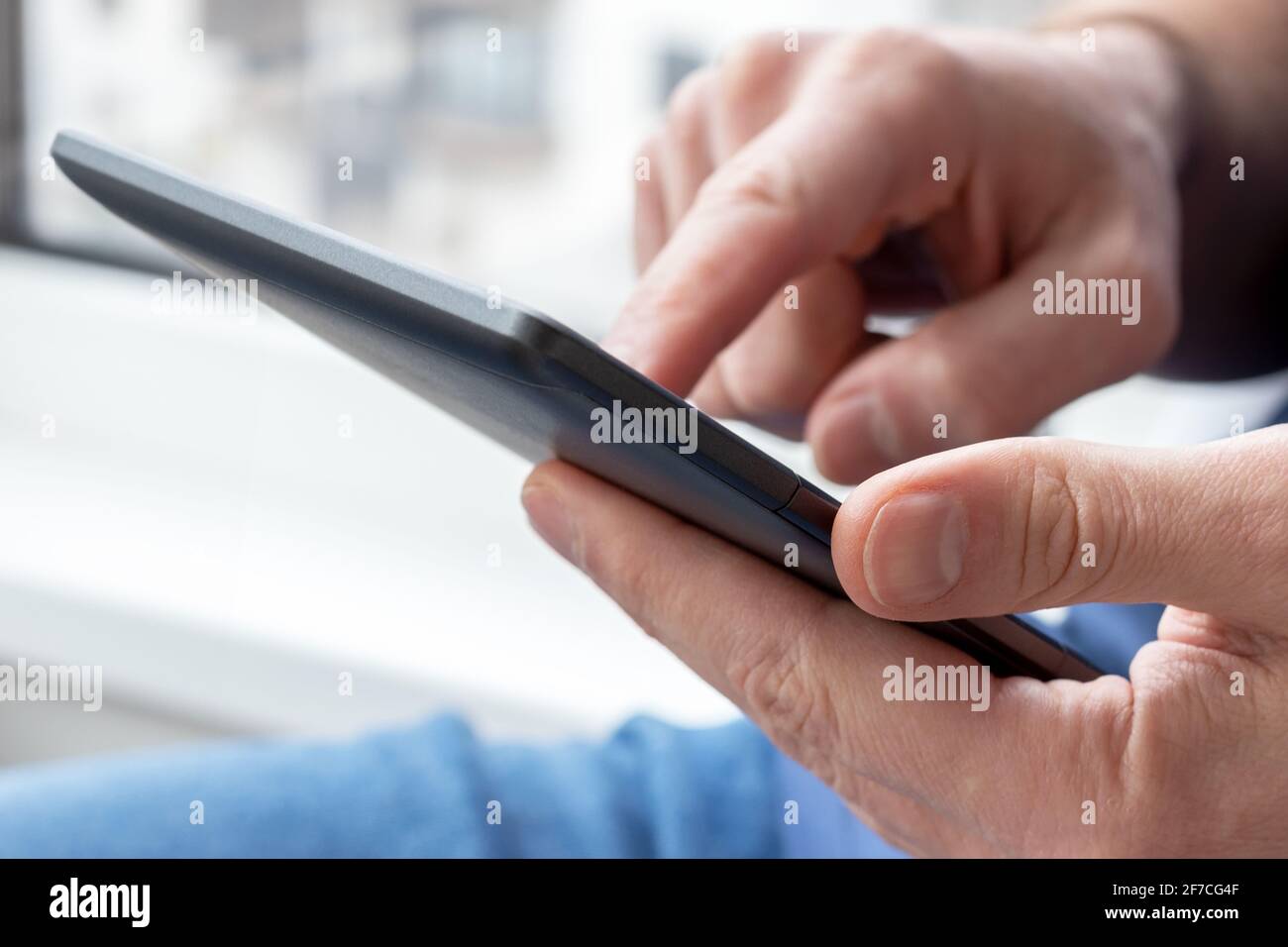 Gray e-reader electronic book in male hands. A man in with a tablet against a blurred background. Selective focus Stock Photo