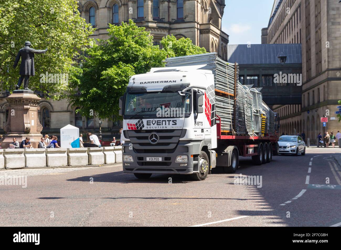 A Mercedes-Benz Actros 1844 truck hauls an articulated flat trailer carrying portable crowd control barriers away from Albert Square, Manchester. Stock Photo
