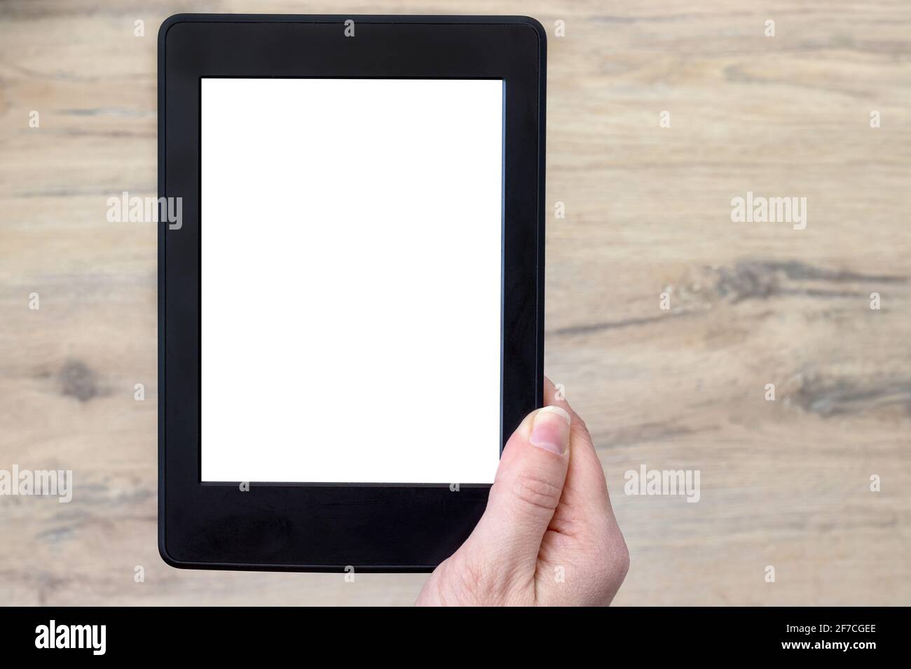 A modern black electronic book with a white blank screen in female hand against a blurred wooden floor background. Mockup tablet closeup Stock Photo