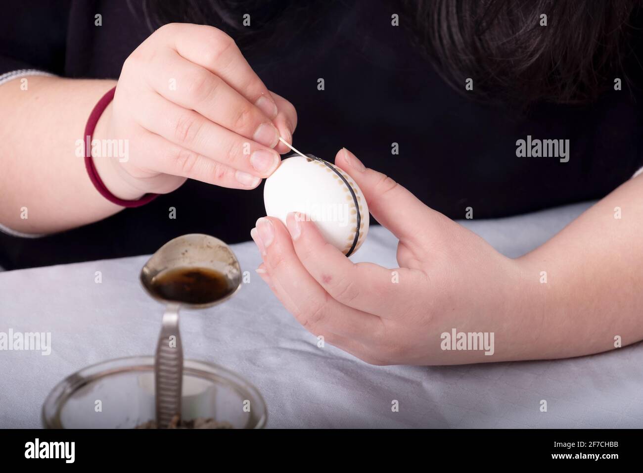 Female hands paints a white Easter egg according to german Sorbian tradition with a trimmed goose quill and melted bees wax along a rubber ring Stock Photo